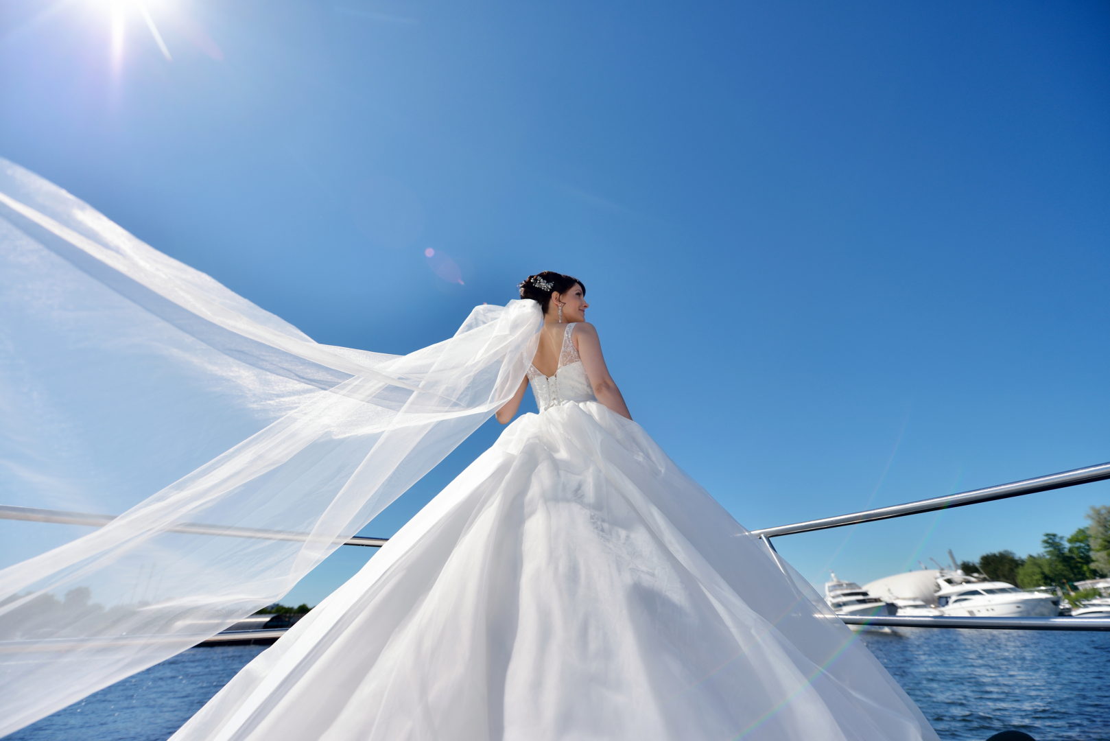 Beauty bride in bridal gown with lace veil on a yacht. Beautiful model girl in a white wedding dress. Female portrait on the nature. Woman with hairstyle. Cute lady outdoors