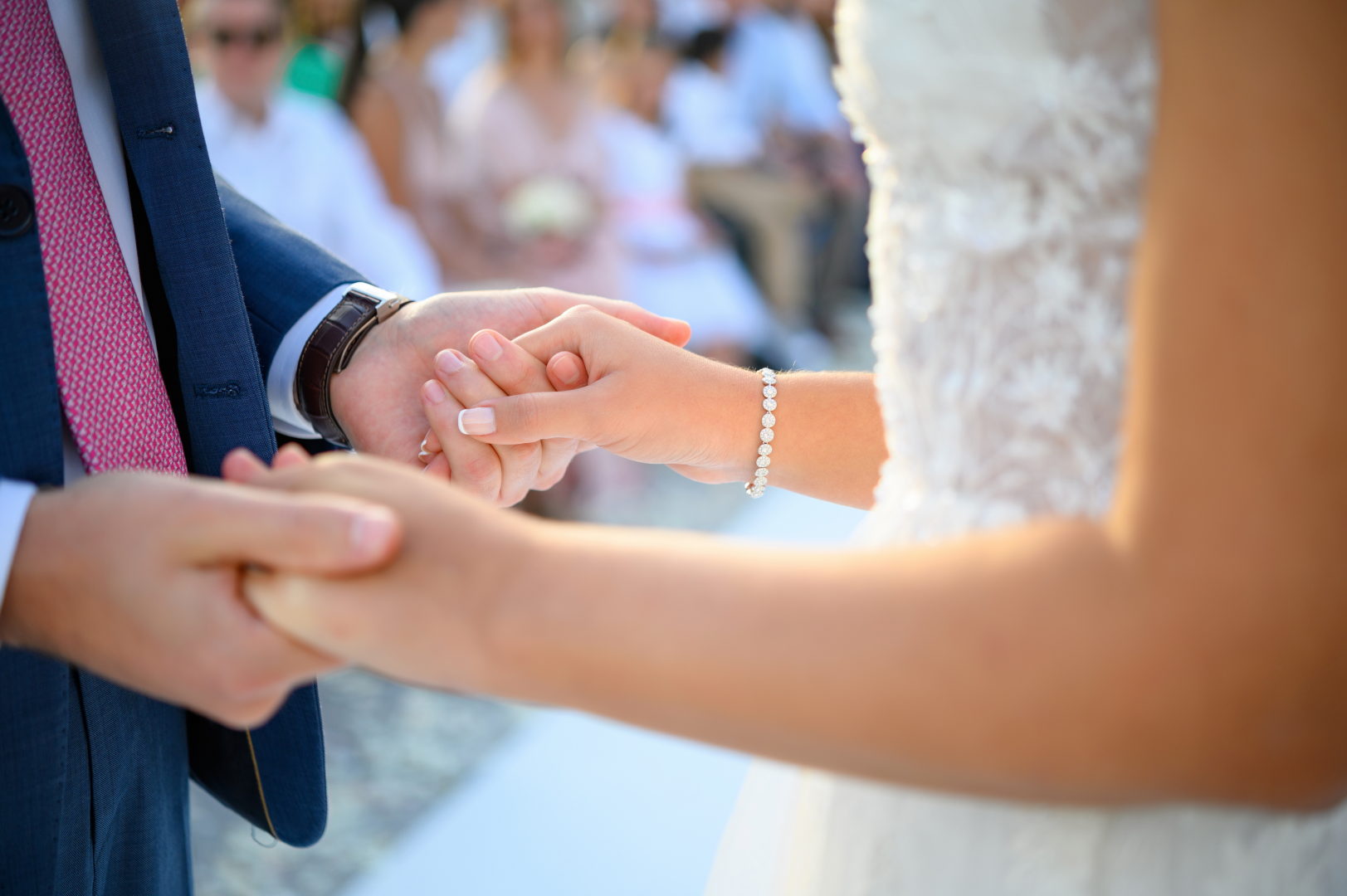 Crop unrecognizable romantic wedding couple in festive outfits holding hands together during ceremony on street with guests on blurred background