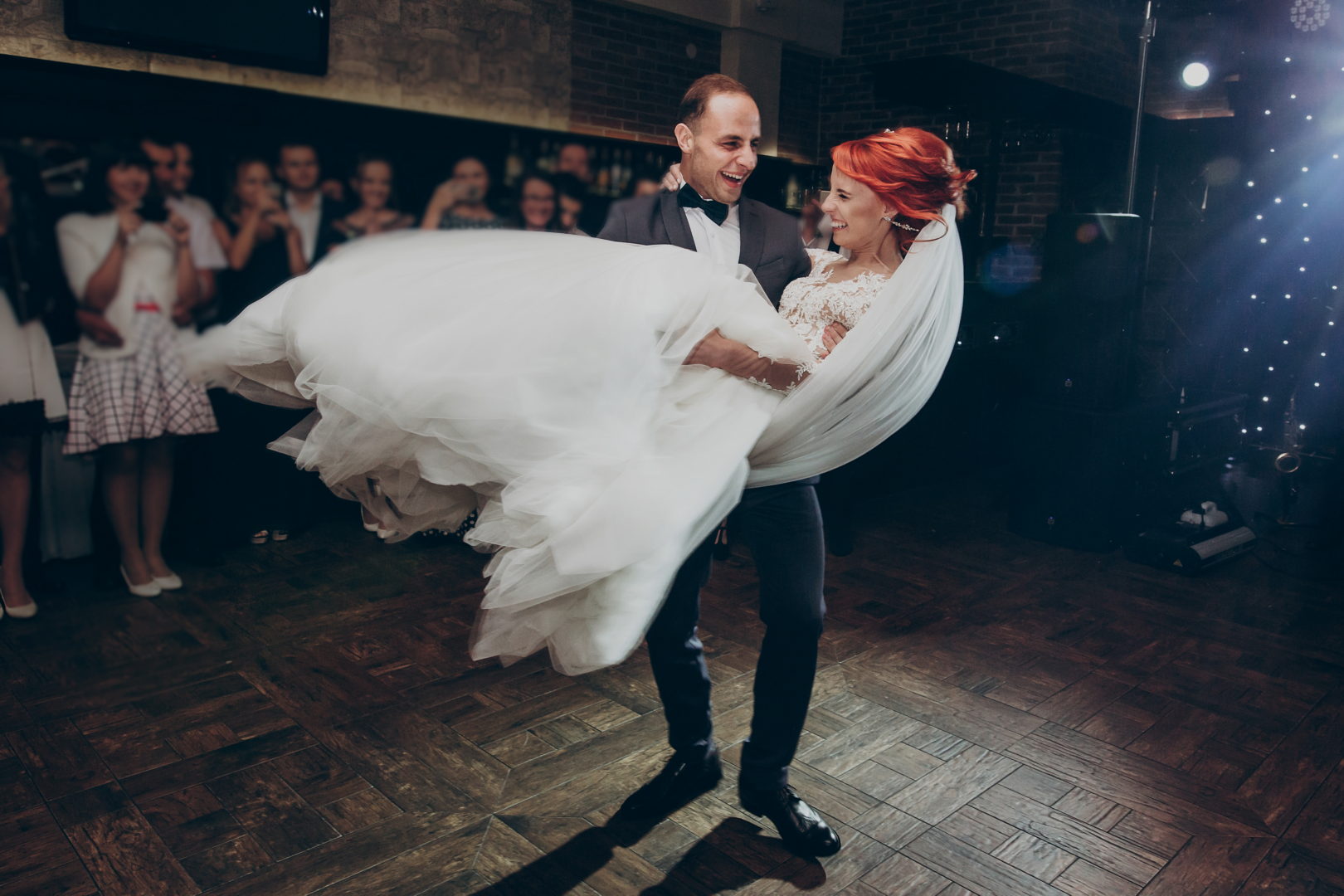 stylish groom lifting happy bride and  dancing at wedding reception in light. gorgeous wedding couple performing first dance in restaurant. newlyweds, emotional moment. space for text